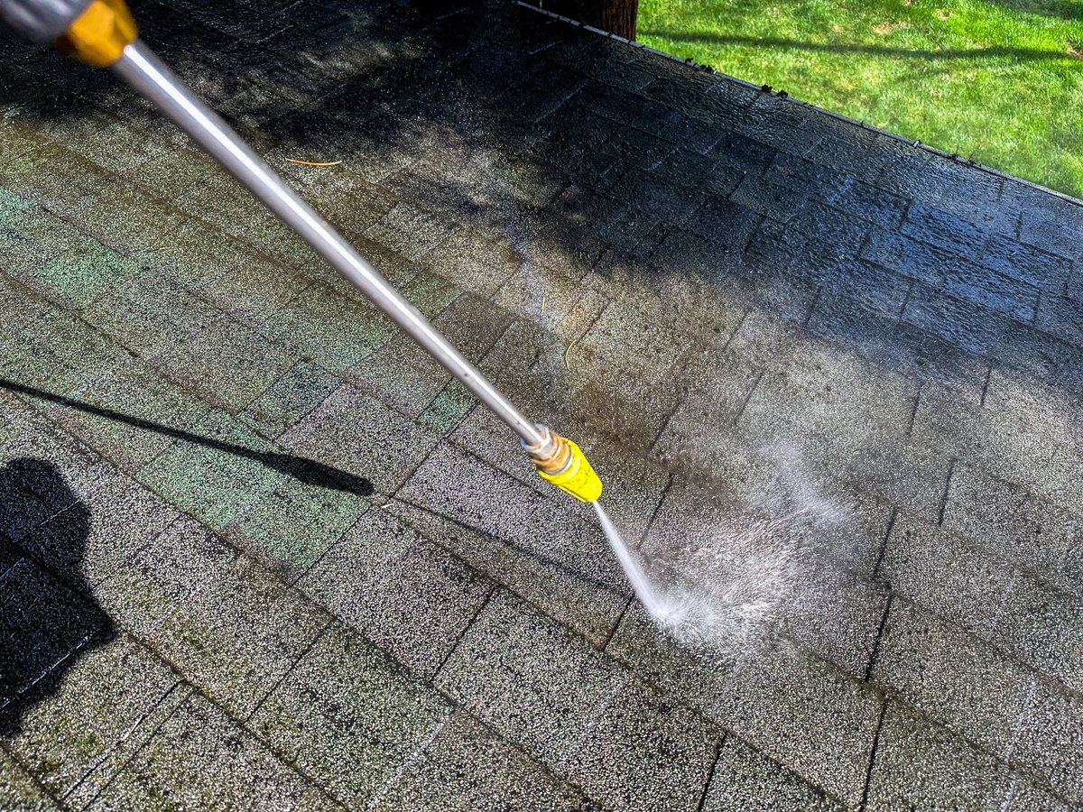 Pressure washer clearing debris from a house exterior on a clear day