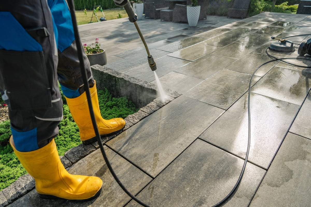 JTR Services technician pressure washing a stone patio on a sunny day